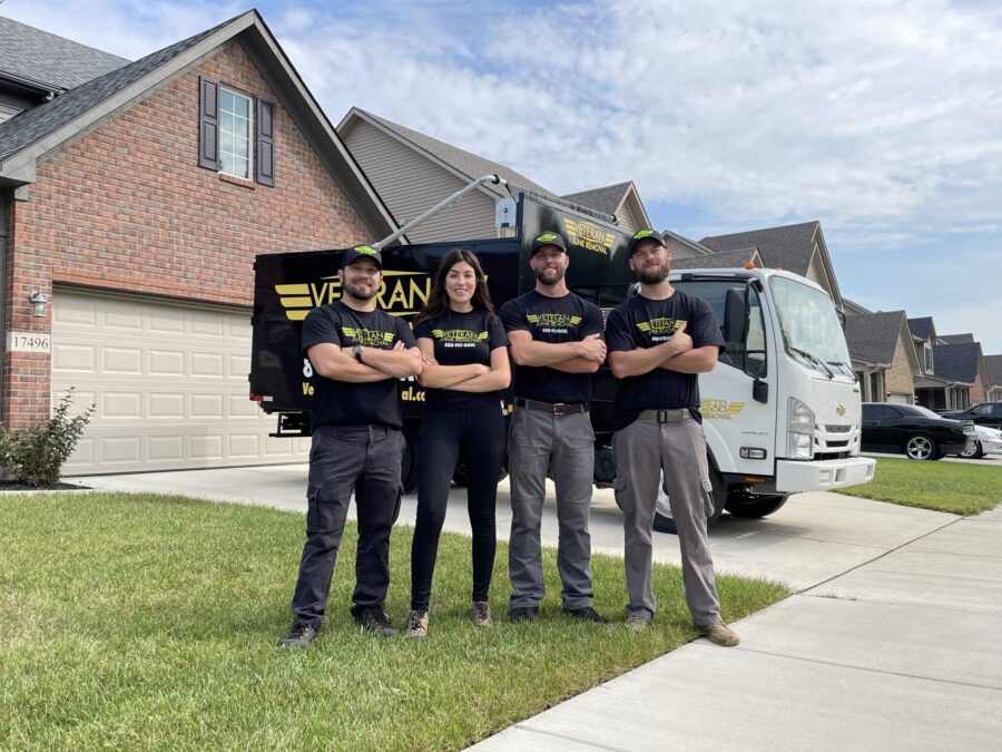 Four Veteran Junk Removal team members standing on a front lawn with the branded truck in the driveway behind them