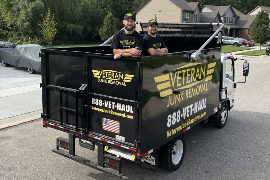 Two Veteran Junk Removal crew members standing in the back of the branded truck