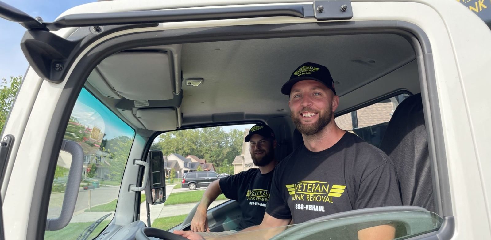 A smiling Veteran Junk Removal driver at the wheel with a crew member beside him