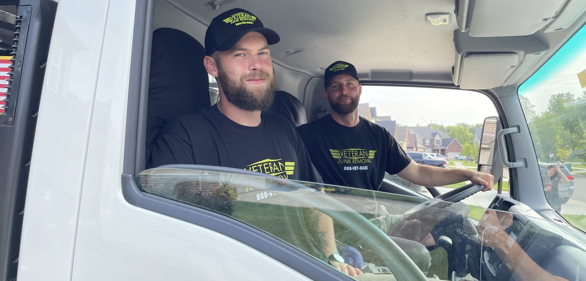 Two Veteran Junk Removal crew members in the truck cab, seen through the driver's window