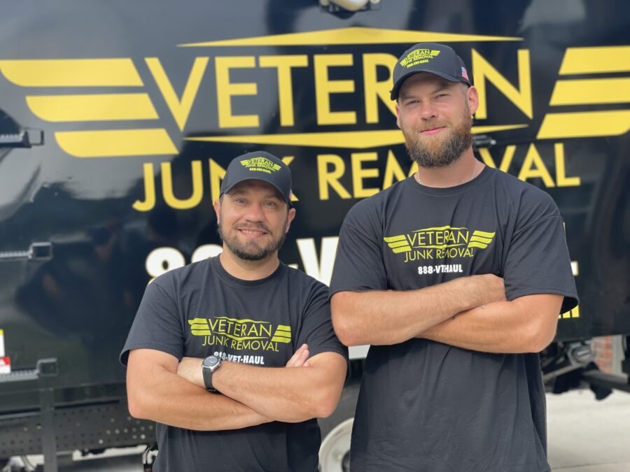 Two Veteran Junk Removal crew members with arms crossed in front of the truck's winged logo