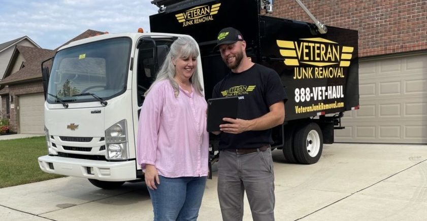 A Veteran Junk Removal crew member going over a tablet with a customer beside the truck