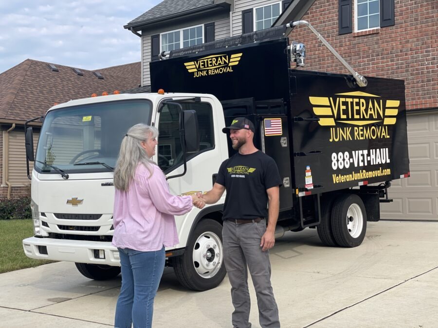 A Veteran Junk Removal crew member shaking hands with a homeowner beside the branded truck